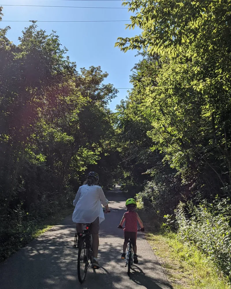 A parent and child riding side by side down a tree-lined trail